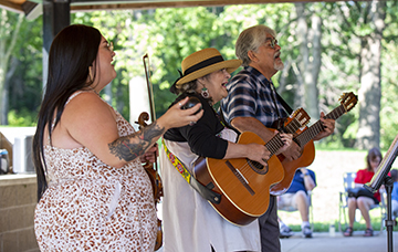 Two people playing the guitar with one person holding a violin while clapping. 