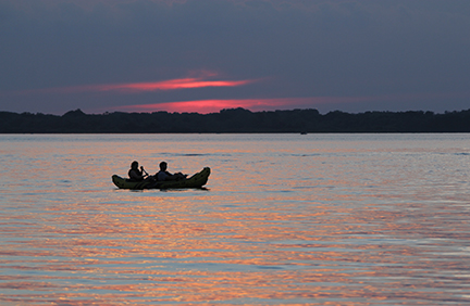 A silhouette of two people in a canoe on Lake Byllesby at dusk.